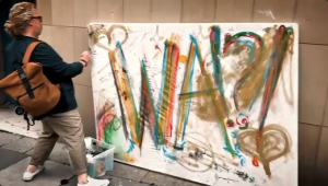 Photo of a man painting WA!?! on a giant canvas outside