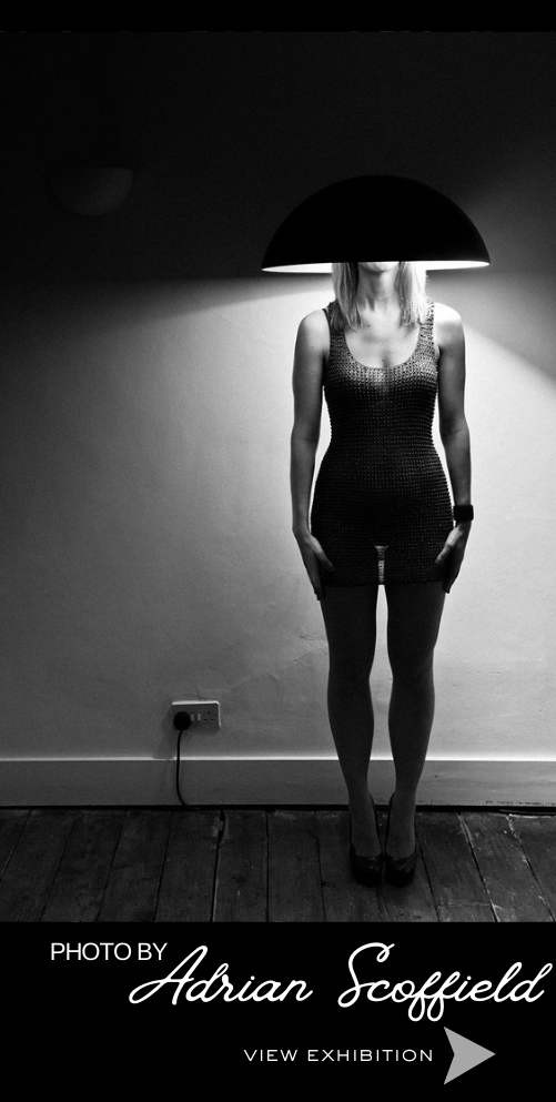 Black and White photo of a woman with a lampshade on her head. Photo by Adrian Scoffield -View Exhibition
