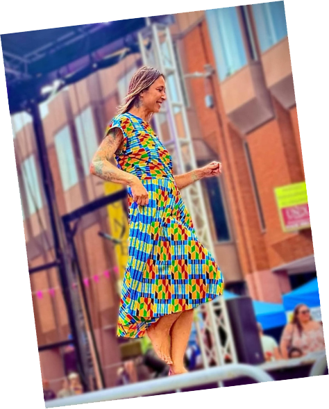 Itchy Valentine walking a catwalk wearing a long dress with a blue, green, yellow and red pattern.
